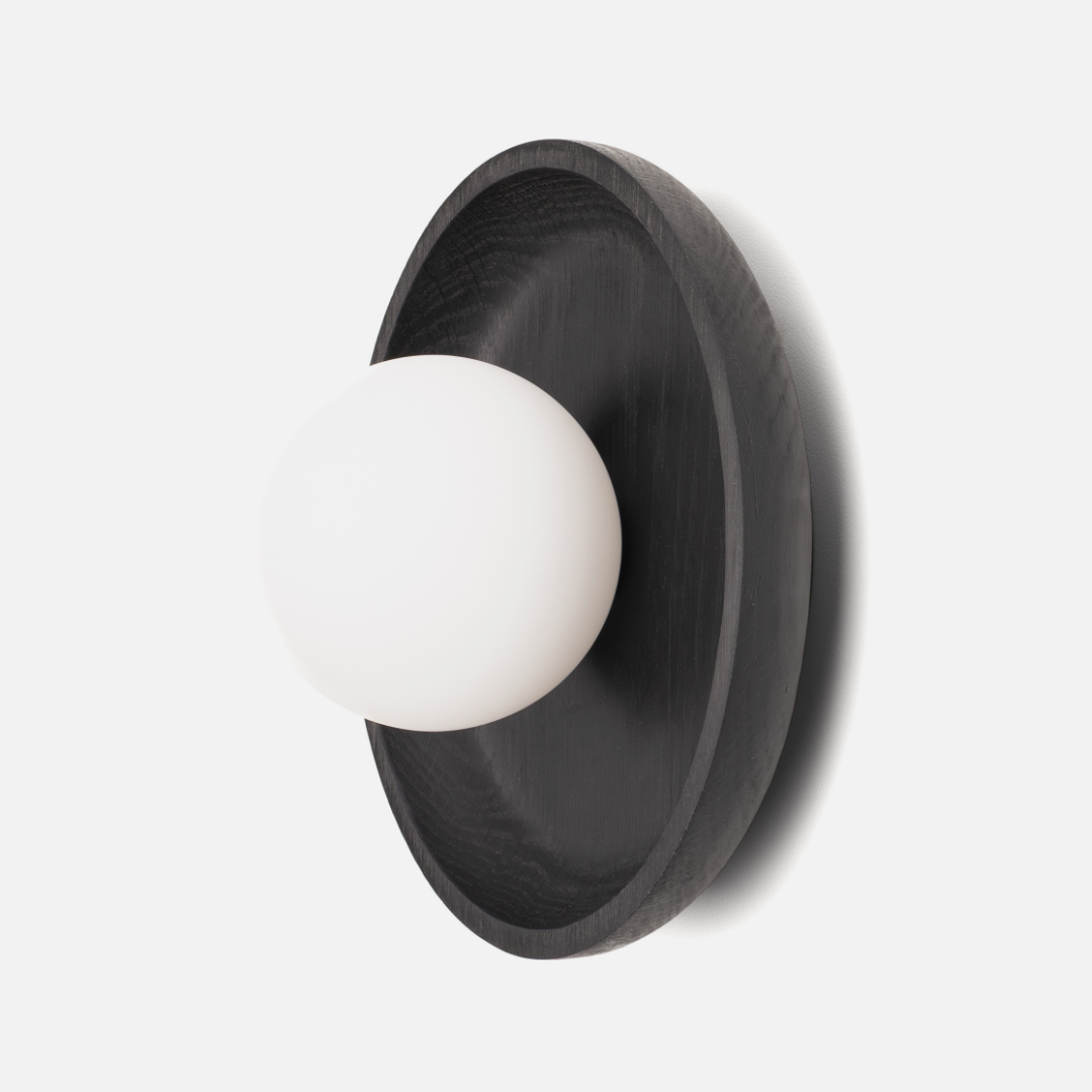 Wall-mounted light fixture with black circular shade and white bulb on a light gray background