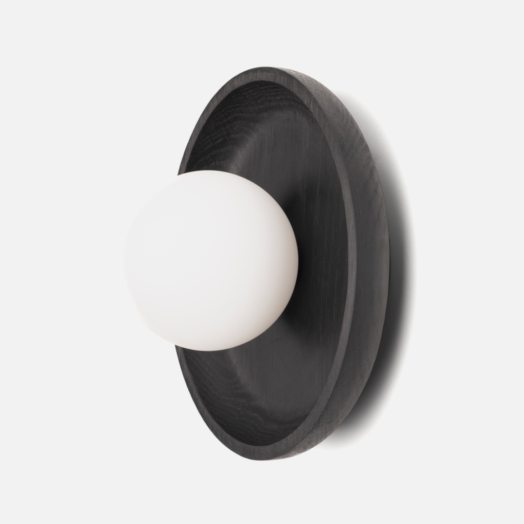 Wall-mounted light fixture with black circular shade and white bulb on a light gray background