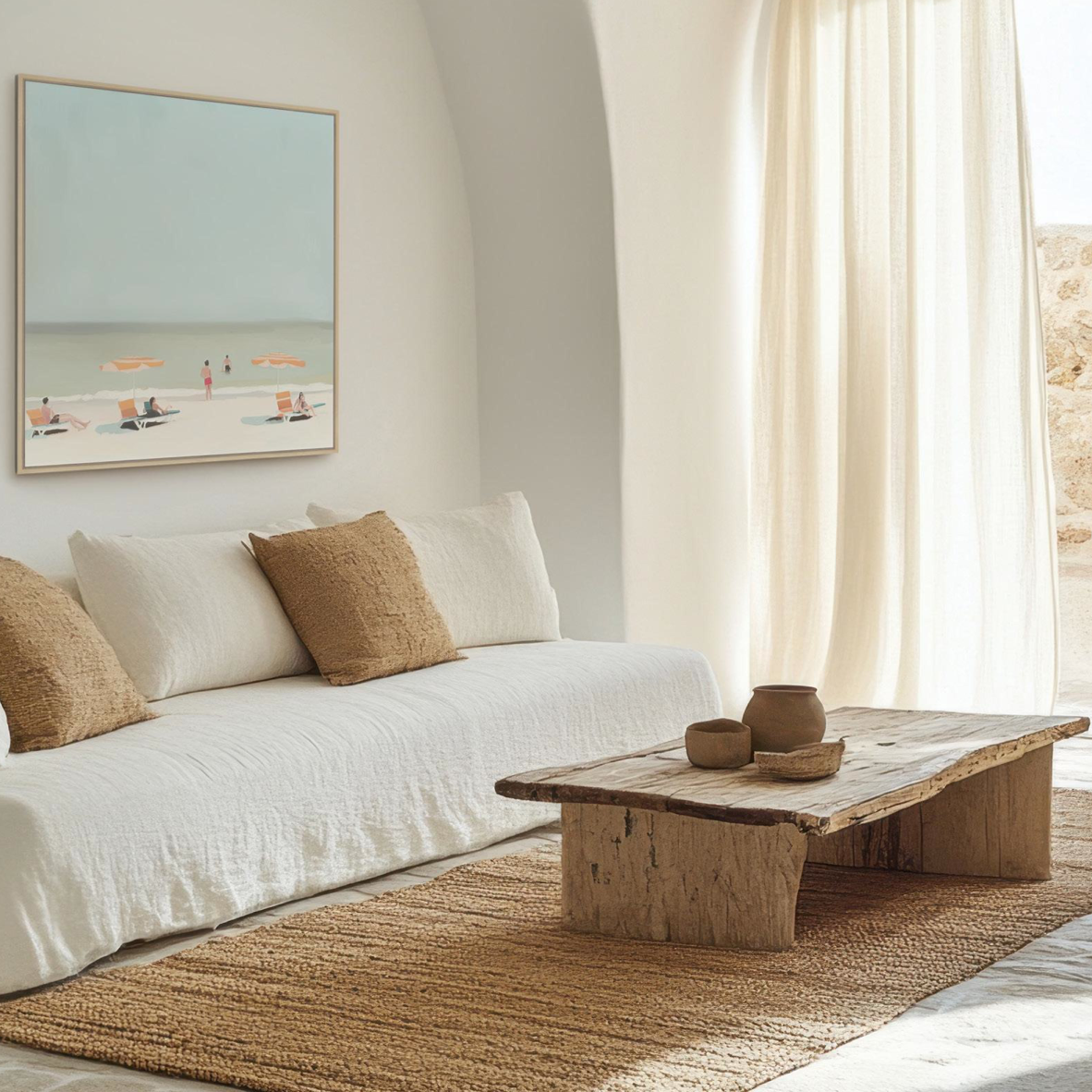A styled living room scene featuring a white upholstered daybed with textured beige pillows, a rustic wooden coffee table, a woven jute rug, and a framed beach art print on the wall.