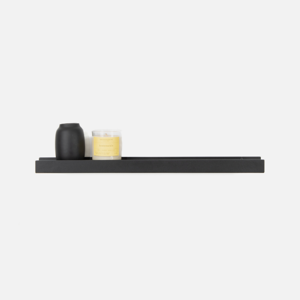 A medium-sized, wall-mounted black metal lip shelf with a few items placed on it, against a white background.
